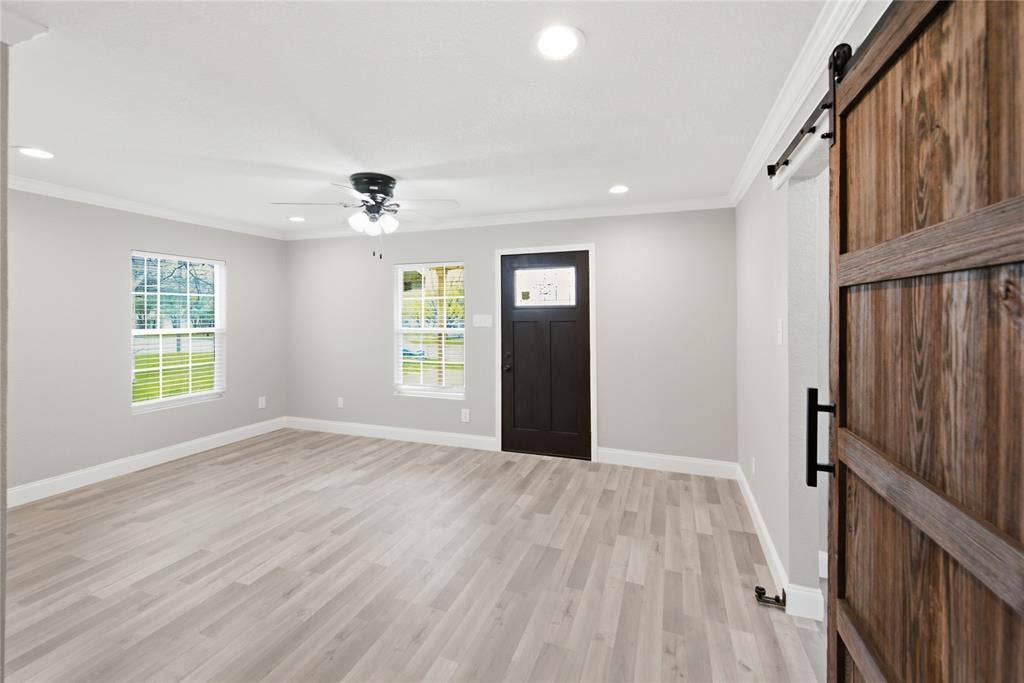 Interior space featuring wood-finish flooring, recessed lighting, a ceiling fan with integrated light fixture, windows with white trim, and a wooden sliding barn door with black hardware