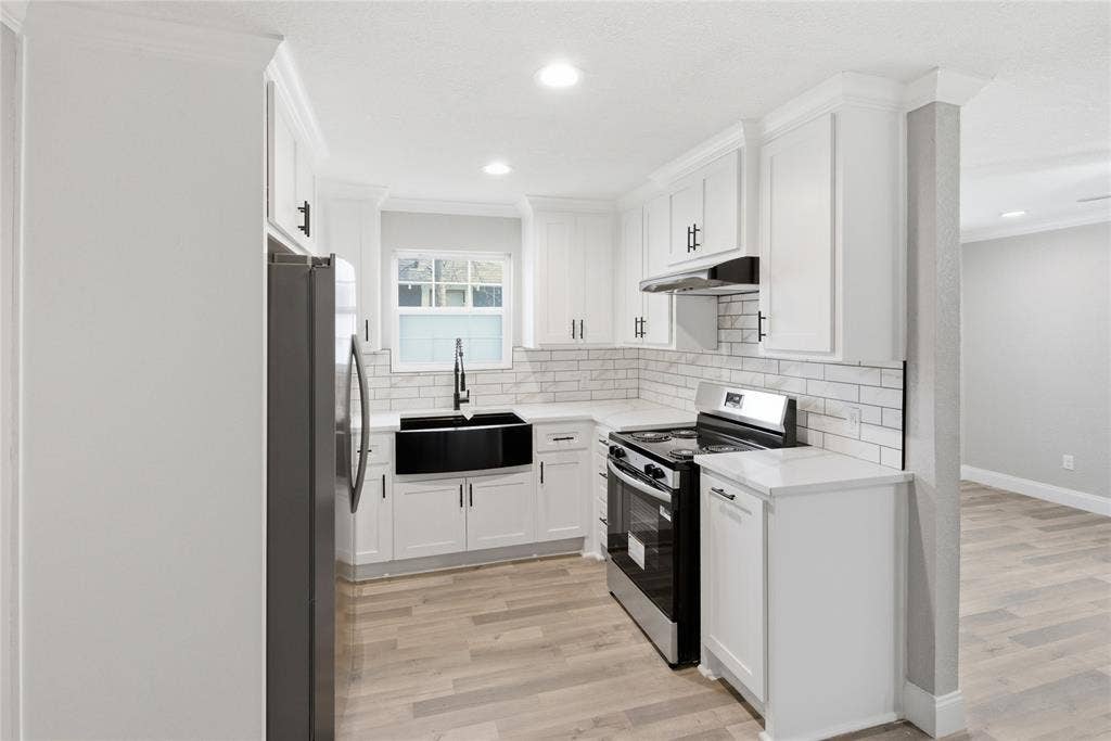 Kitchen featuring white shaker-style cabinetry, light-toned countertop surfaces, white subway tile backsplash, farmhouse-style apron sink with a high-arch faucet, and wood-finish flooring