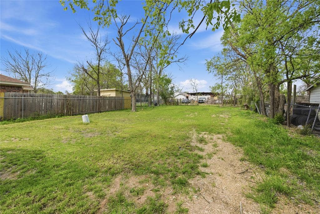 Expansive backyard featuring mature trees, partial wood fencing, and a chain-link perimeter