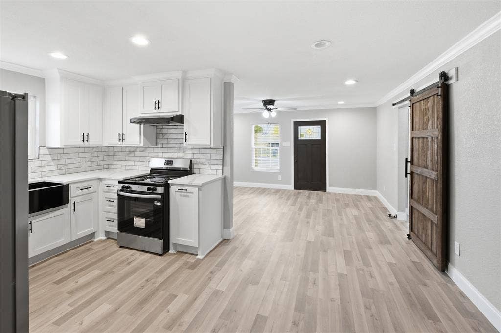 Kitchen featuring white shaker-style cabinetry, a light-toned tile backsplash, wood-finish flooring, and a sliding barn-style door