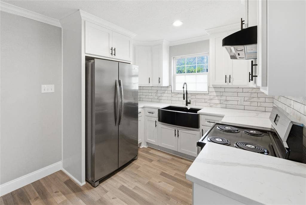 Kitchen featuring white cabinetry with matte black hardware, stone-finish countertops, subway tile backsplash, farmhouse-style sink with a pull-down faucet, and wood-finish flooring