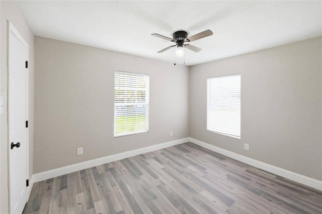 Room featuring wood-finish flooring, two windows with horizontal blinds, neutral wall paint, and a ceiling fan with integrated light fixture