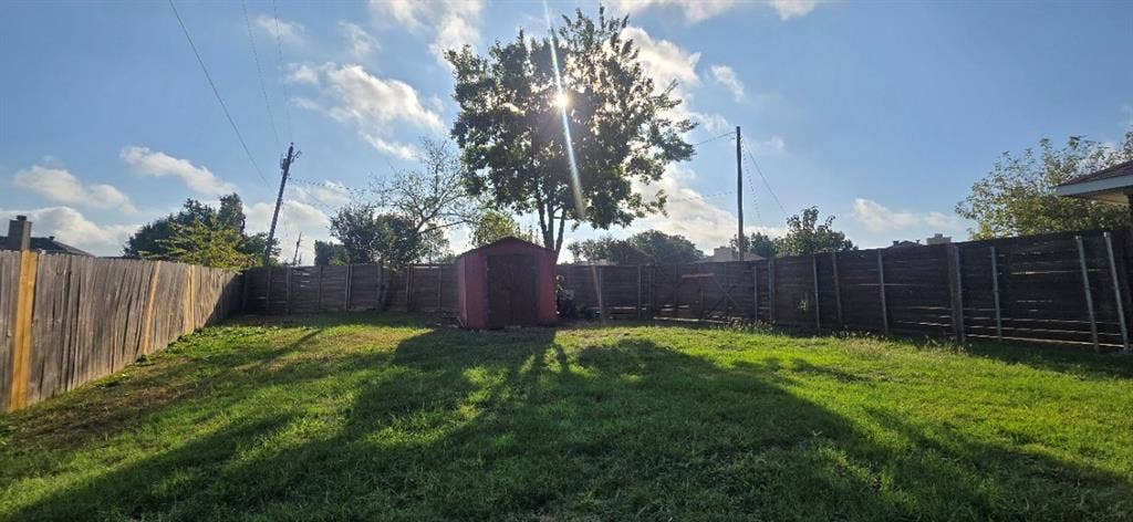Backyard featuring a grass lawn, perimeter wood fencing, and a detached storage structure