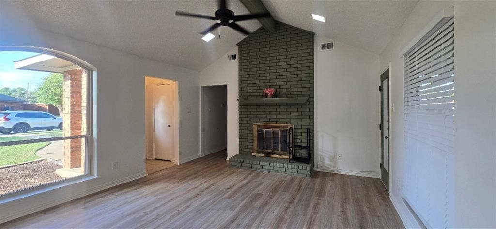 Vaulted ceilings, wood-finish flooring, brick-faced fireplace with a mantel, skylights, and ceiling fan