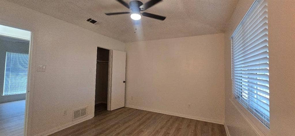 Neutral interior room featuring wood-finish flooring, a ceiling fan with integrated lighting, and horizontal window blinds
