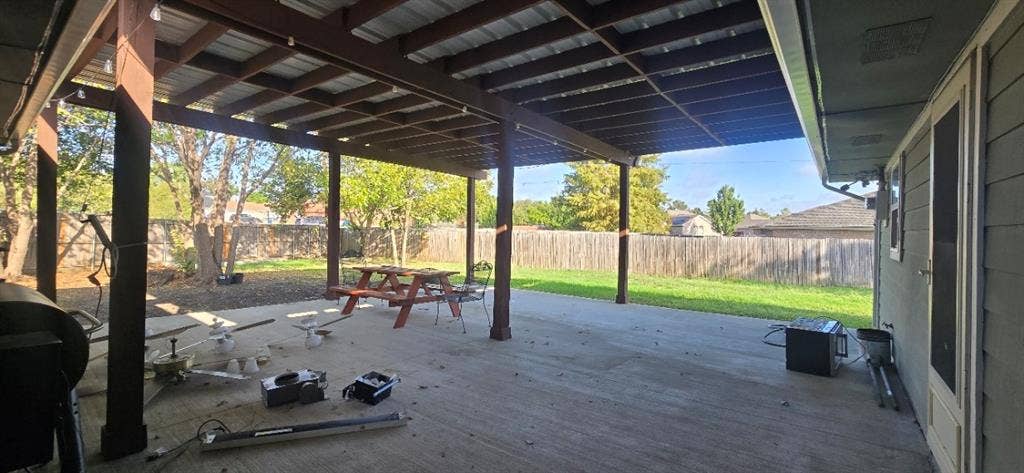 Covered patio featuring an exposed beam ceiling, concrete flooring, support columns, and a fenced backyard