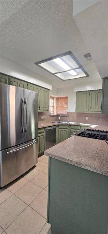 Kitchen featuring sage green cabinetry, solid surface countertops, stainless steel refrigerator, tile flooring, and a recessed ceiling light fixture
