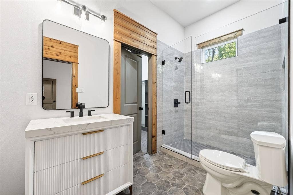 116 Carolynn Road, Mabank, TX 75156 Bathroom featuring a fluted vanity with a stone countertop, walk-in shower with floor-to-ceiling tile, frameless glass enclosure, matte black fixtures, and hexagonal floor tile