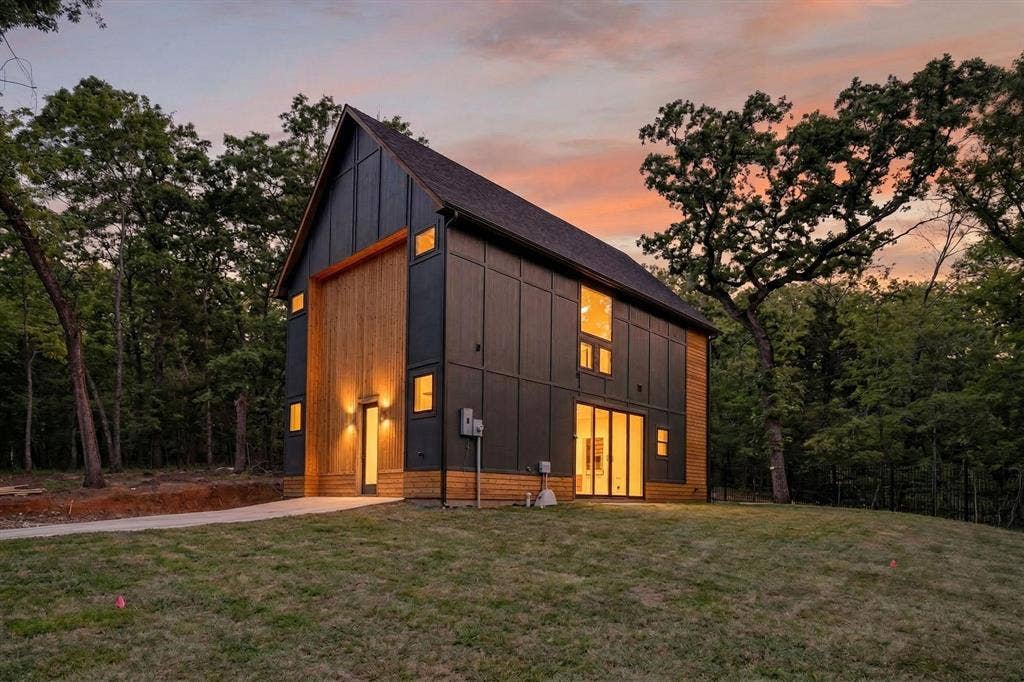 116 Carolynn Road, Mabank, TX 75156 Modern two-story architectural exterior featuring dark panel siding, natural wood-finish vertical accents, a steeply pitched roof, and large glass entry doors