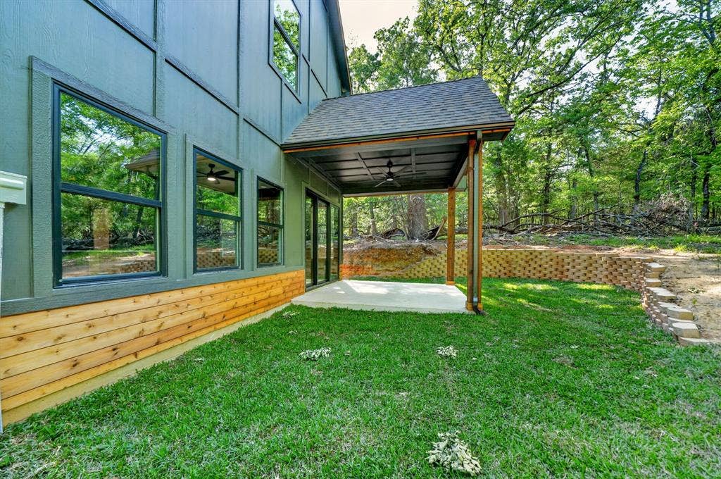 116 Carolynn Road, Mabank, TX 75156 Exterior featuring board and batten siding with natural wood-plank accents, a covered patio with a ceiling fan, a concrete slab, and a multi-tiered stone retaining wall
