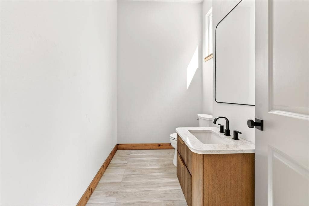 116 Carolynn Road, Mabank, TX 75156 Bathroom vanity featuring a natural wood-finish cabinet, stone-top surface with an integrated sink, matte black widespread faucet, and a coordinating framed rectangular mirror
