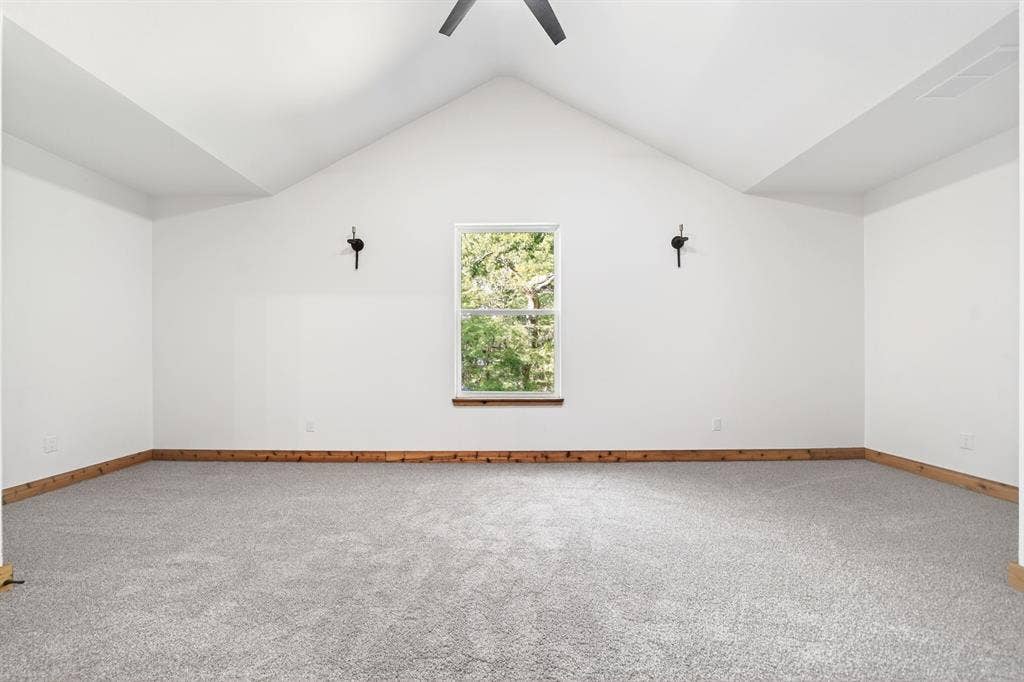 116 Carolynn Road, Mabank, TX 75156 Vaulted ceiling featuring a central ceiling fan, neutral wall-to-wall carpeting, wood trim detailing, and dual wall-mounted light fixtures