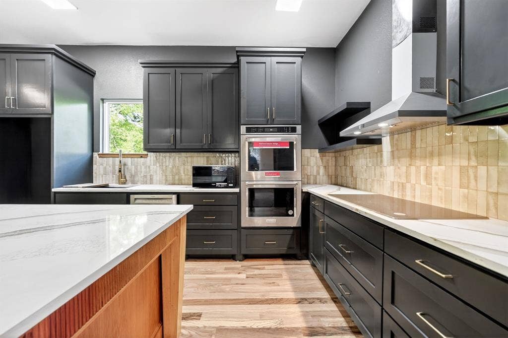 116 Carolynn Road, Mabank, TX 75156 Kitchen featuring dark cabinetry, stone-finish countertops, stainless steel double wall ovens, a tile backsplash, and wood-finish flooring