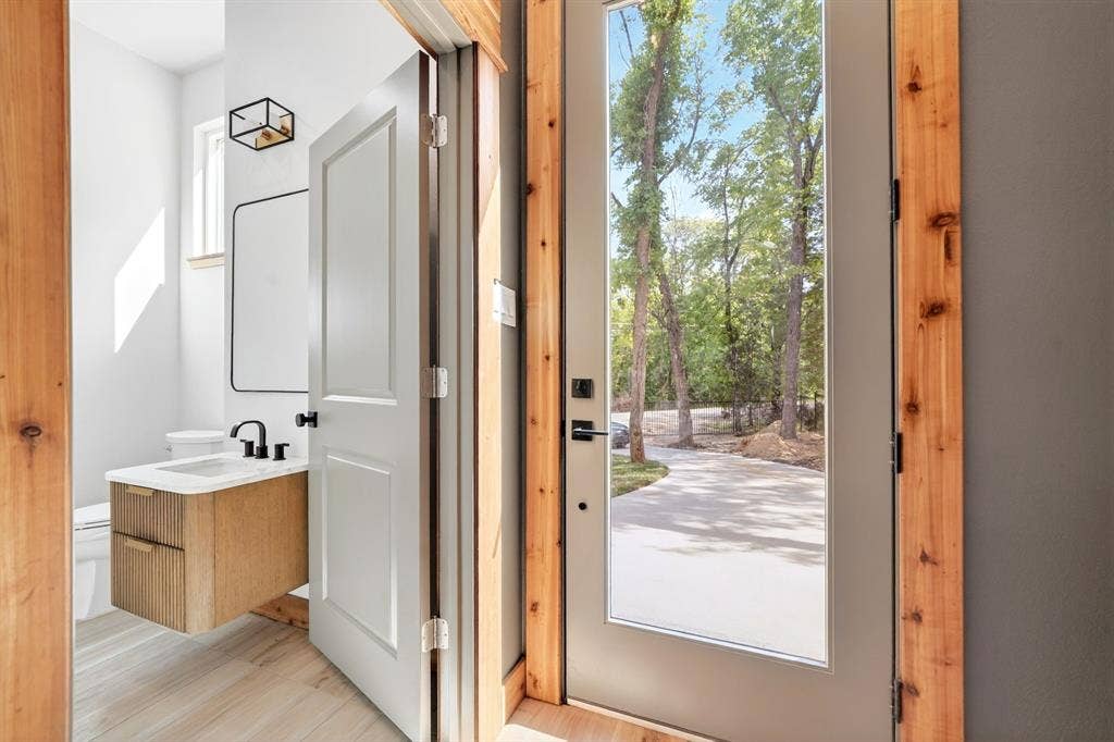 116 Carolynn Road, Mabank, TX 75156 Modern half-bath featuring a floating wood-finish vanity, rectangular vessel sink, matte black faucet, and geometric wall-mounted light fixture, complemented by an entry door with natural wood casing