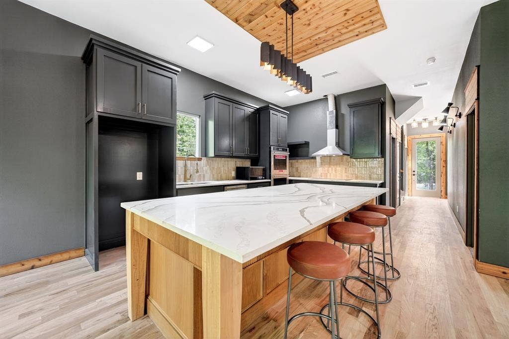 116 Carolynn Road, Mabank, TX 75156 Kitchen featuring an expansive center island with a stone-surface countertop, ceiling-mounted wood inlay detail, charcoal-toned cabinetry, stainless steel wall-mounted range hood, and light-tone wood-finish flooring