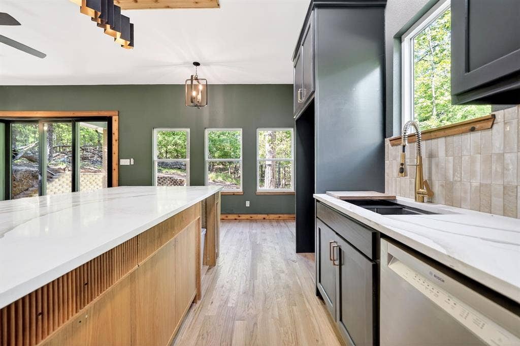 116 Carolynn Road, Mabank, TX 75156 Kitchen featuring an expansive center island with fluted wood cabinetry and solid-surface countertops, custom charcoal-toned cabinetry, light-toned wood-finish flooring, textured subway tile backsplash, and metallic pull-down faucet