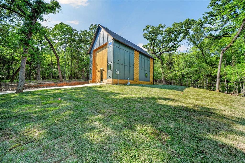 116 Carolynn Road, Mabank, TX 75156 Modern architectural exterior featuring metal panel siding, vertical wood-finish siding, a steep pitched roofline, and expansive surrounding woodland