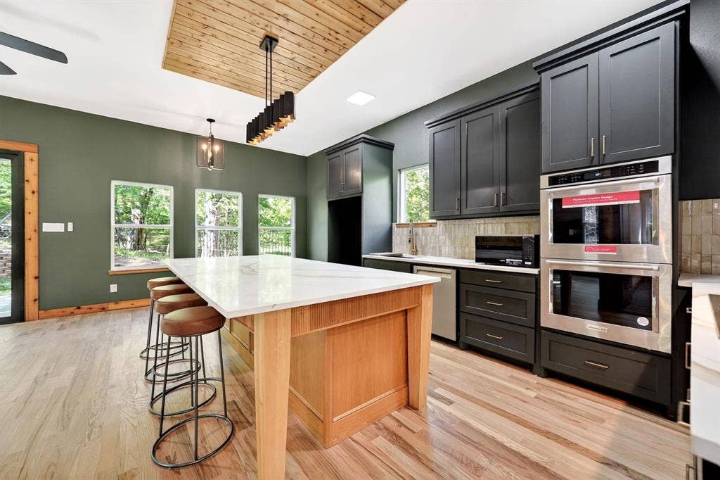 116 Carolynn Road, Mabank, TX 75156 Kitchen featuring a natural-finish wood center island with a stone countertop, dark cabinetry, stainless steel double wall ovens, wood-finish flooring, and a recessed ceiling accent with plank wood detailing