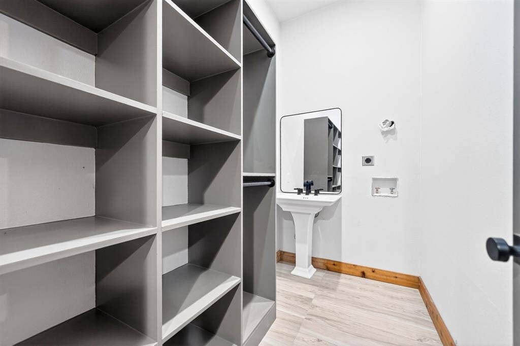 116 Carolynn Road, Mabank, TX 75156 Built-in grey custom shelving, pedestal sink with matte black faucet, wall-mounted rectangular mirror, and wood-finish flooring