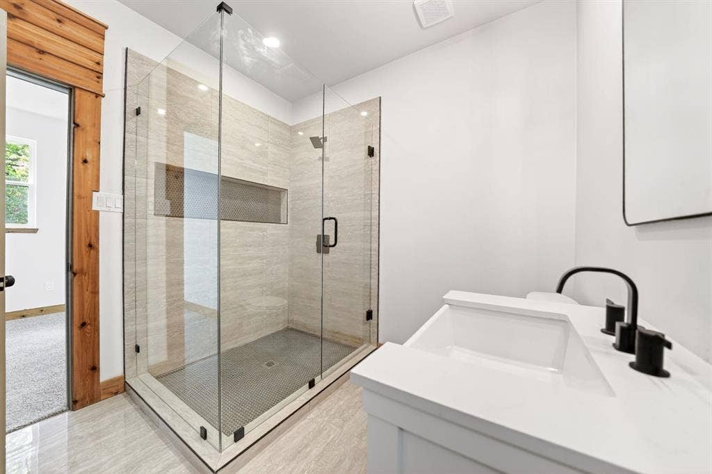116 Carolynn Road, Mabank, TX 75156 Frameless glass-enclosed shower with tiled walls and built-in niche, white vanity cabinet with stone-finish countertop, and matte black plumbing fixtures