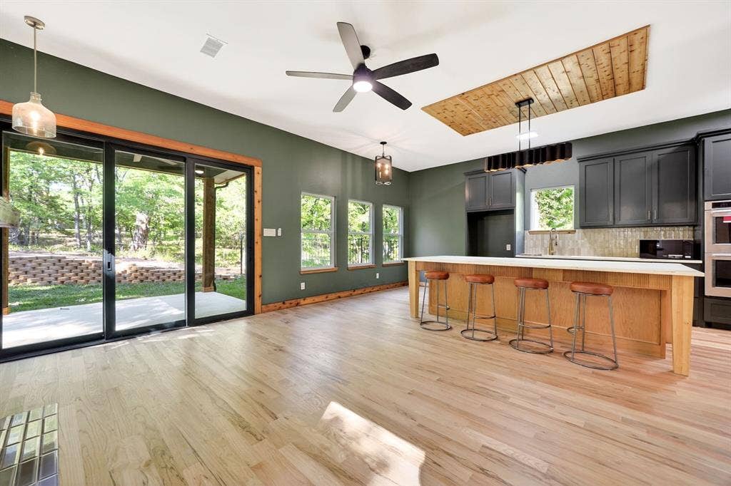 116 Carolynn Road, Mabank, TX 75156 Open-concept kitchen featuring an expansive center island with seating, wood-finish flooring, custom cabinetry, a wood-paneled ceiling inlay, and sliding glass doors
