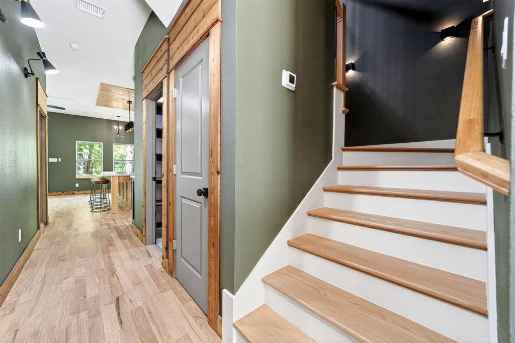 116 Carolynn Road, Mabank, TX 75156 Interior staircase with natural wood treads, white risers, and a matching wood-finish handrail, complemented by natural wood door trim, wood-finish flooring, and wall-mounted task lighting