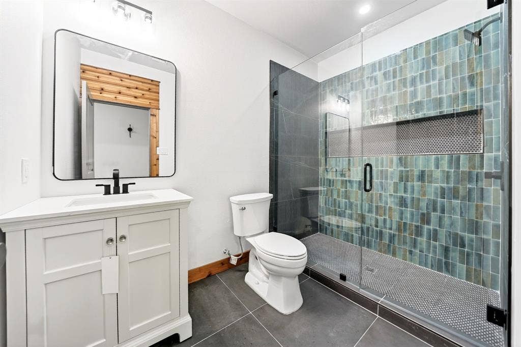 116 Carolynn Road, Mabank, TX 75156 Bathroom featuring a white vanity with a rectangular sink, a frameless glass-enclosed shower with teal vertical tiling, a built-in shower niche, and dark large-format floor tile