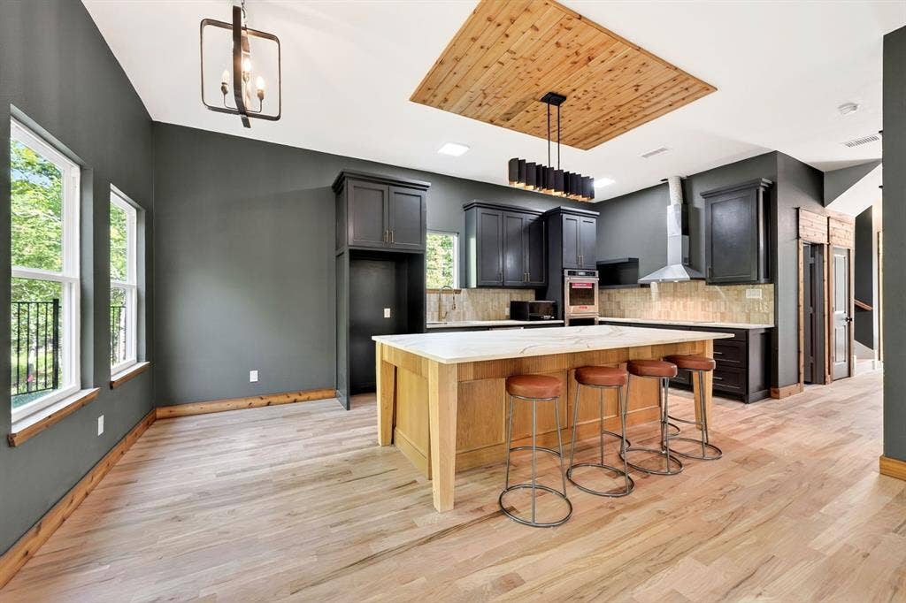 116 Carolynn Road, Mabank, TX 75156 Kitchen featuring an oversized island with a stone-top surface, wood-finish flooring, custom cabinetry with dark finish, a wood-paneled ceiling inset, and stainless steel hood range