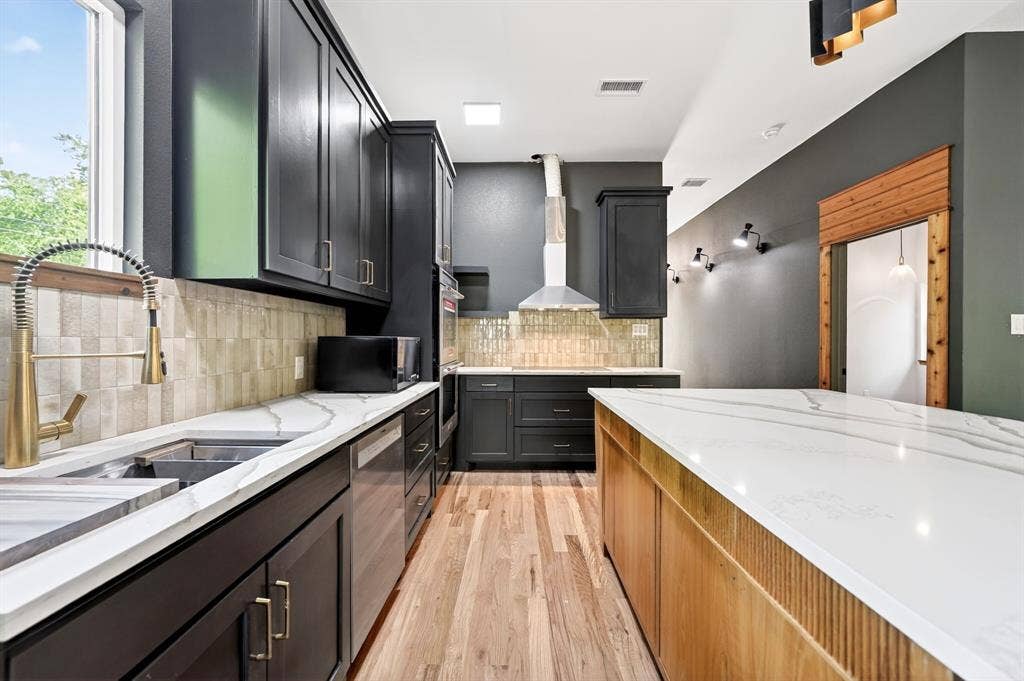 116 Carolynn Road, Mabank, TX 75156 Kitchen featuring dark cabinetry, expansive stone-surface countertops, wood-finish flooring, a stainless steel range hood, and a dual-handle bridge faucet