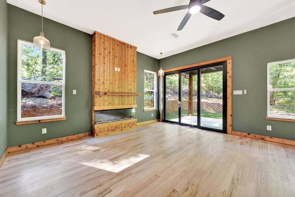 116 Carolynn Road, Mabank, TX 75156 Living area featuring wood-finish flooring, a floor-to-ceiling wood-paneled fireplace, glass sliding doors, dual pendant lighting, and a ceiling fan