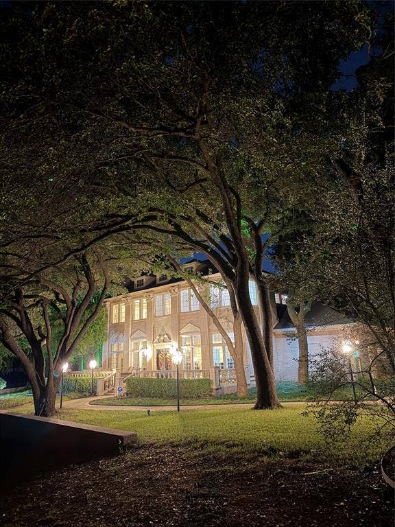 3011 Country Club Drive, McKinney, TX 75070 Two-story brick exterior featuring a stone balustrade, mature canopy trees, manicured landscaping, and integrated exterior lighting
