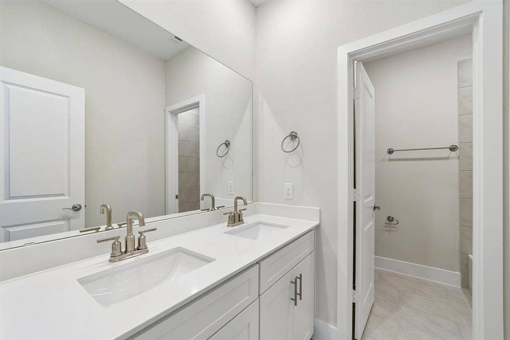 11512 Empress Drive, Frisco, TX 75035 Dual-sink vanity with a solid-surface countertop, white Shaker-style cabinetry, polished metal hardware, and a large-format vanity mirror