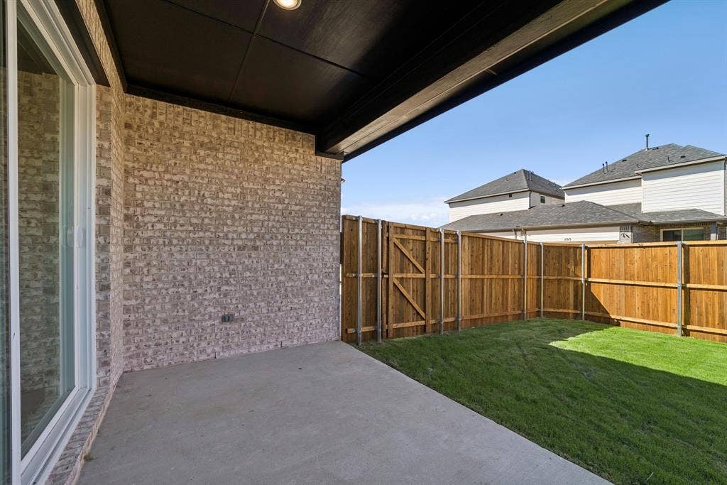 11512 Empress Drive, Frisco, TX 75035 Covered concrete patio featuring a brick exterior wall, recessed lighting, and a wood privacy fence bordering the lawn