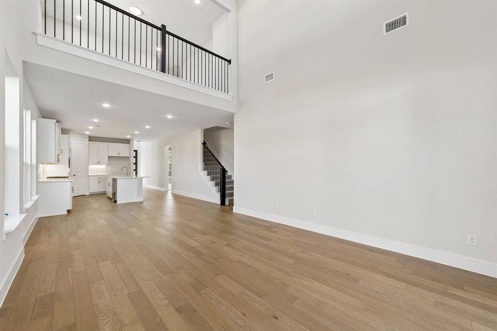 11512 Empress Drive, Frisco, TX 75035 Two-story volume ceiling with a mezzanine overlook, wood-finish flooring, recessed lighting, and a kitchen featuring built-in cabinetry and a central island