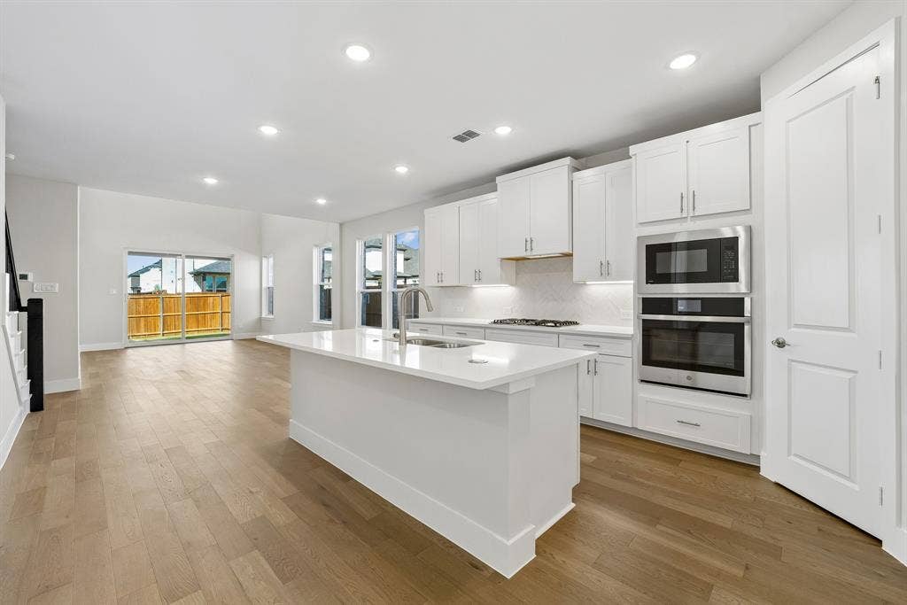 11512 Empress Drive, Frisco, TX 75035 Kitchen featuring white cabinetry, quartz countertops, a central island with an undermount sink, built-in stainless steel appliances, and wood-finish flooring