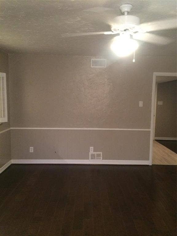 1217 Cloverdale Drive, Richardson, TX 75080 Dark-toned wood-finish flooring, textured wall surfaces, and white chair rail molding, complemented by a ceiling fan with integrated lighting and plantation-style window shutters
