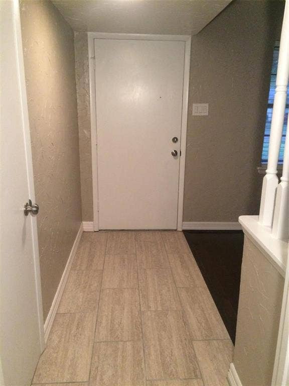 1217 Cloverdale Drive, Richardson, TX 75080 Entry area featuring light-toned rectangular floor tile, neutral textured wall finishes, a solid core white entry door with metallic hardware, and a white balustrade