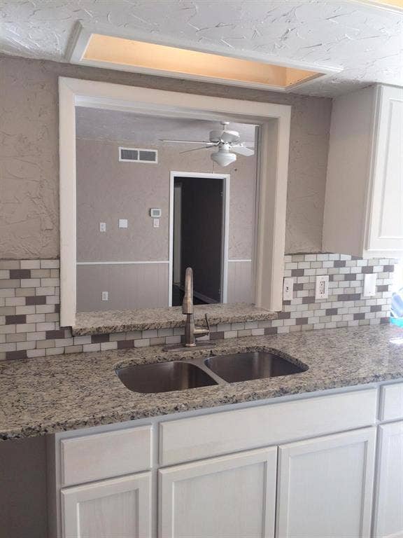1217 Cloverdale Drive, Richardson, TX 75080 Kitchen featuring a stone-composite countertop, dual-basin stainless steel sink with a high-arch faucet, white shaker-style cabinetry, and a multi-tone mosaic tile backsplash