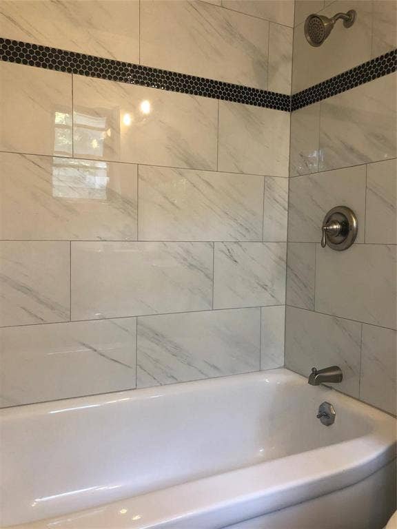 1217 Cloverdale Drive, Richardson, TX 75080 Bathtub enclosure featuring large-format stone-patterned wall tile, a decorative circular mosaic accent border, and brushed metal fixtures