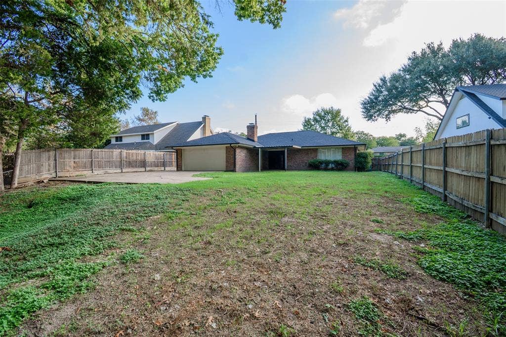 286 Larry Drive, Dallas, TX 75137 Expansive backyard featuring a concrete patio, brick exterior, attached garage, and wood privacy fencing
