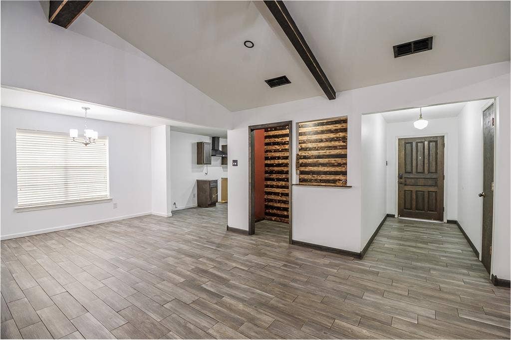 286 Larry Drive, Dallas, TX 75137 Vaulted ceilings with exposed structural beams, wood-finish tile flooring, a multi-paneled wood entry door, and a decorative horizontal-slat wall feature