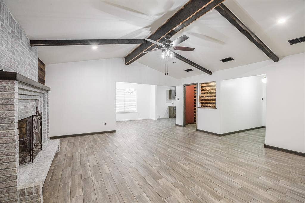 286 Larry Drive, Dallas, TX 75137 Vaulted ceiling with exposed wood beams, brick fireplace featuring a raised hearth, and wood-finish flooring