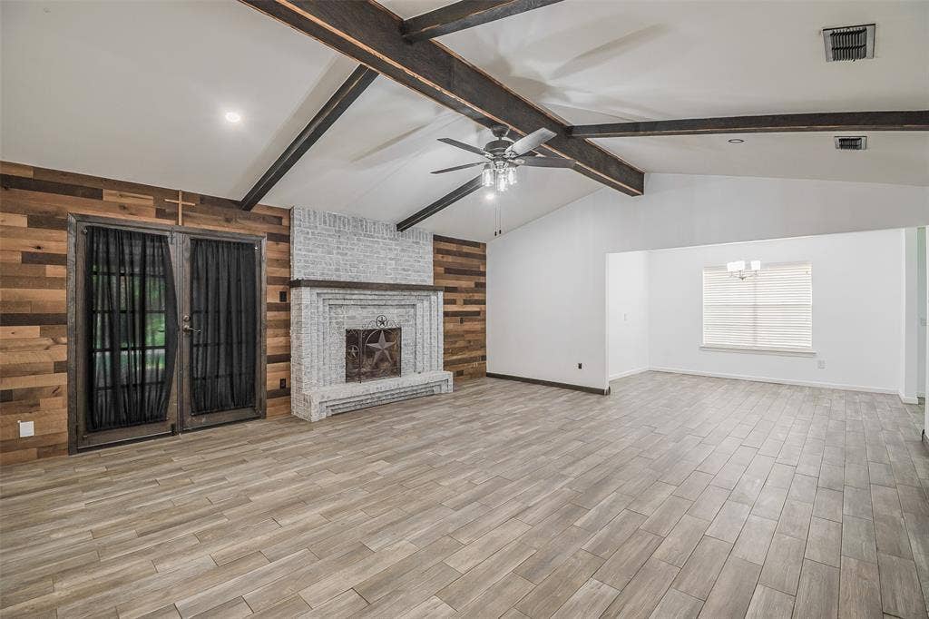 286 Larry Drive, Dallas, TX 75137 Living area featuring a vaulted ceiling with exposed beams, wood-finish flooring, a white-washed brick fireplace, and an accent wall with natural wood planks