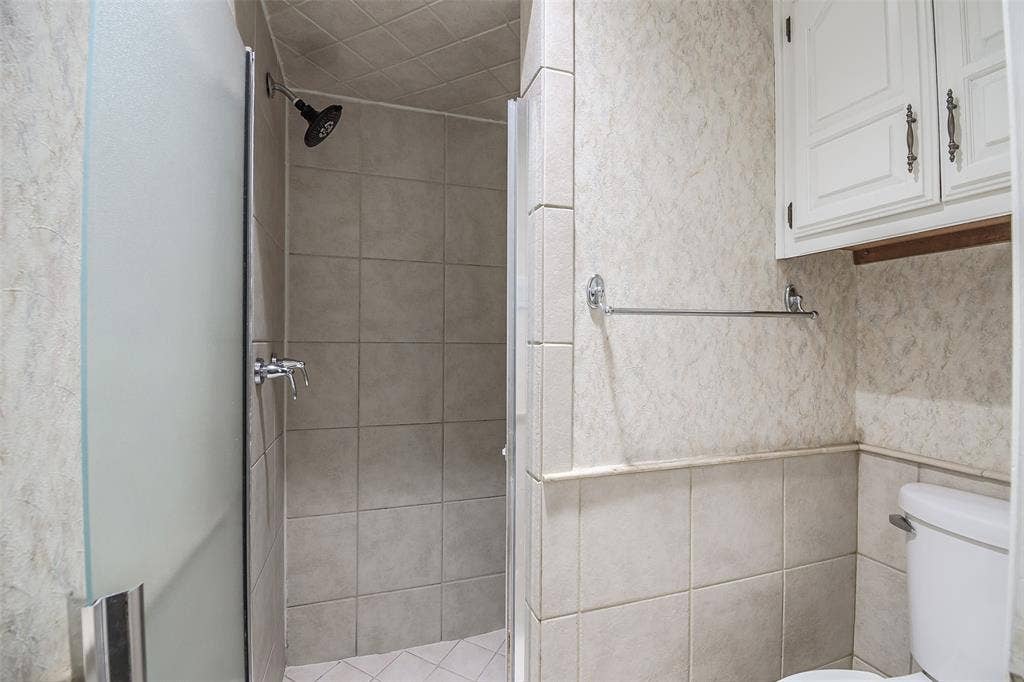 286 Larry Drive, Dallas, TX 75137 Shower enclosure featuring large-format ceramic tile, frosted glass door, and a wall-mounted showerhead, complemented by built-in white cabinetry and a dual-handle faucet