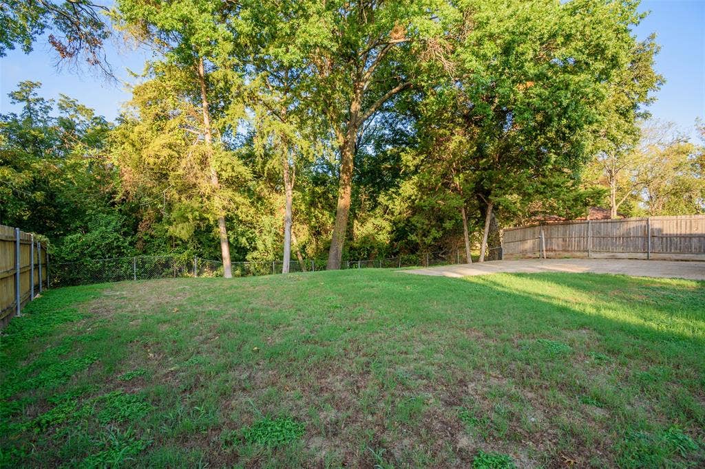 286 Larry Drive, Dallas, TX 75137 Backyard featuring a grass lawn, concrete patio, wooden perimeter fencing, and mature trees