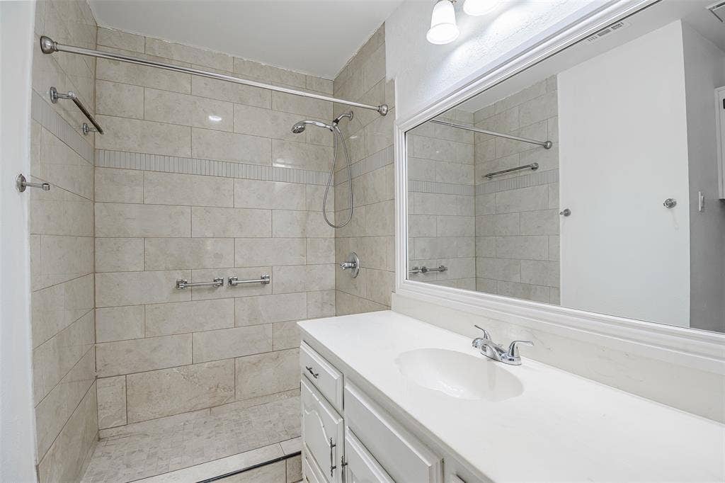 286 Larry Drive, Dallas, TX 75137 Bathroom featuring a walk-in shower with stone-finish tile surround, an integrated handheld shower head, a white cabinetry vanity with a solid-surface countertop, and a large-format vanity mirror with trim detail
