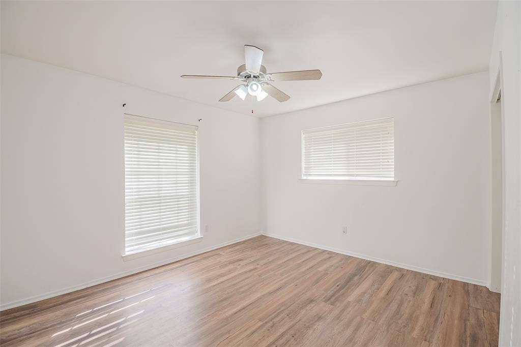 286 Larry Drive, Dallas, TX 75137 Neutral-toned interior featuring wood-finish flooring, two windows with installed blinds, and a central ceiling fan with integrated lighting