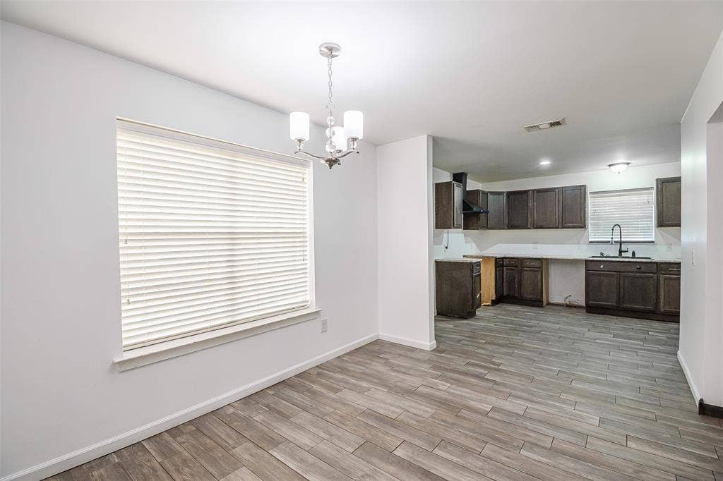 286 Larry Drive, Dallas, TX 75137 Open-concept interior featuring wood-finish flooring, dark-toned cabinetry, a multi-light chandelier, and large windows with integrated blinds