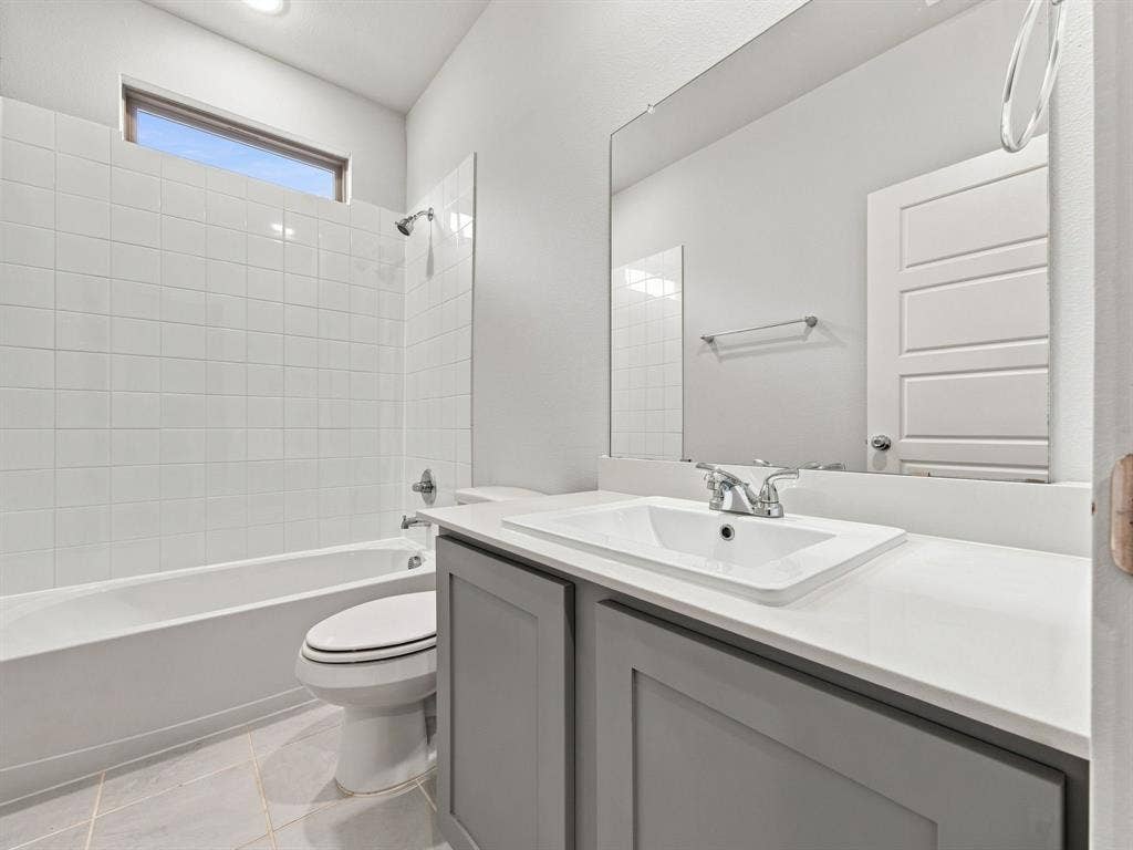 1157 Butterfly Dale Drive, Lavon, TX 75166 Bathroom featuring a grey vanity with a solid surface countertop, undermount sink, full-width mirror, and a tub-shower combination with floor-to-ceiling tile surround and transom window