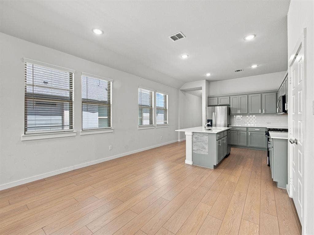 1157 Butterfly Dale Drive, Lavon, TX 75166 Open-concept interior featuring wood-finish flooring, recessed lighting, a center island with a stone-surface countertop, and grey shaker-style cabinetry with tile backsplash